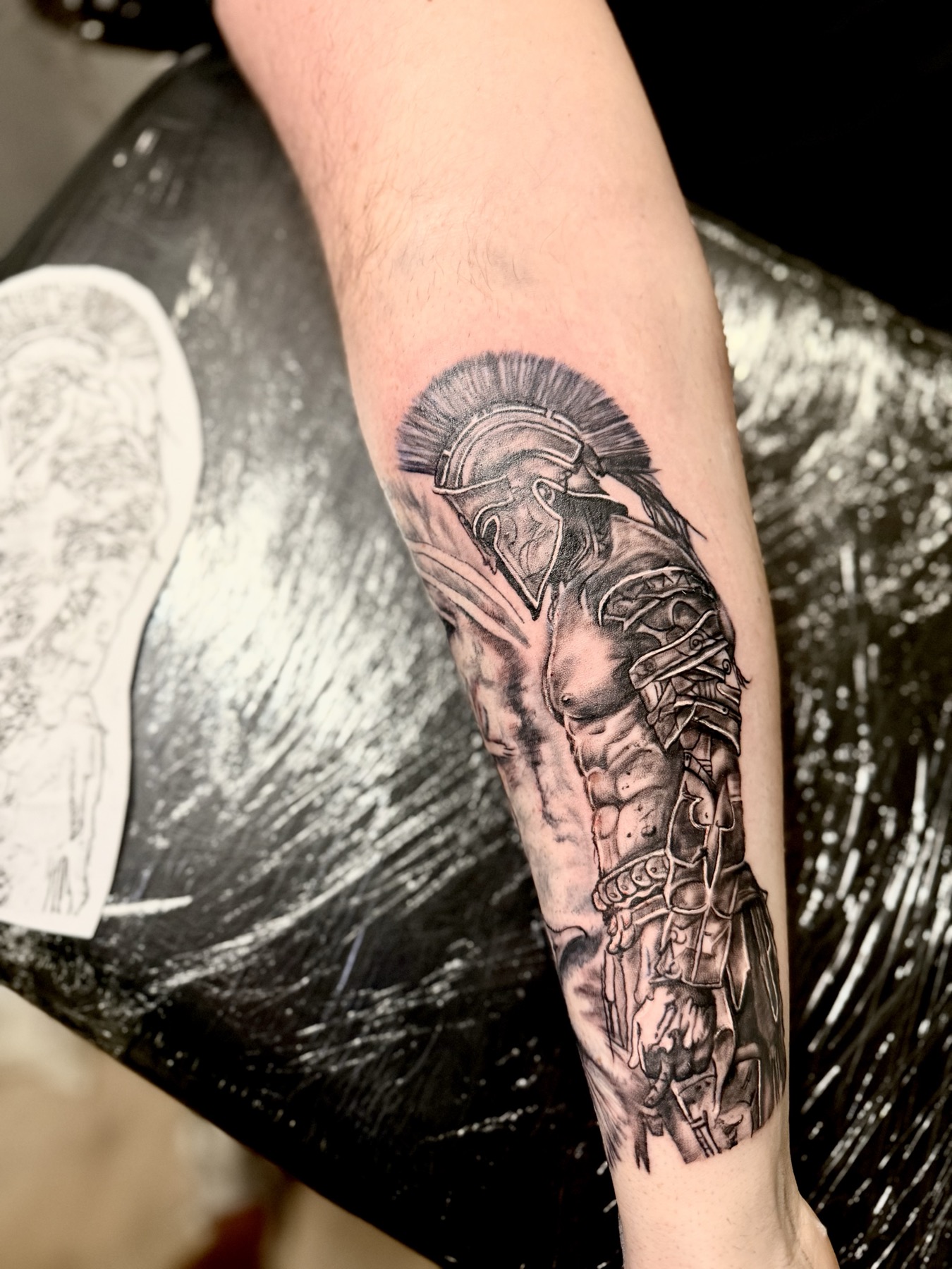 Black and grey realism tattoo of a Spartan warrior on a forearm