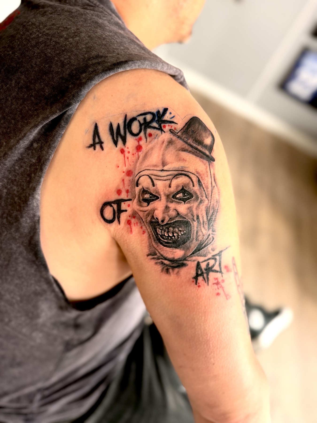 Black and grey horror tattoo of Art the Clown with red accents on a shoulder