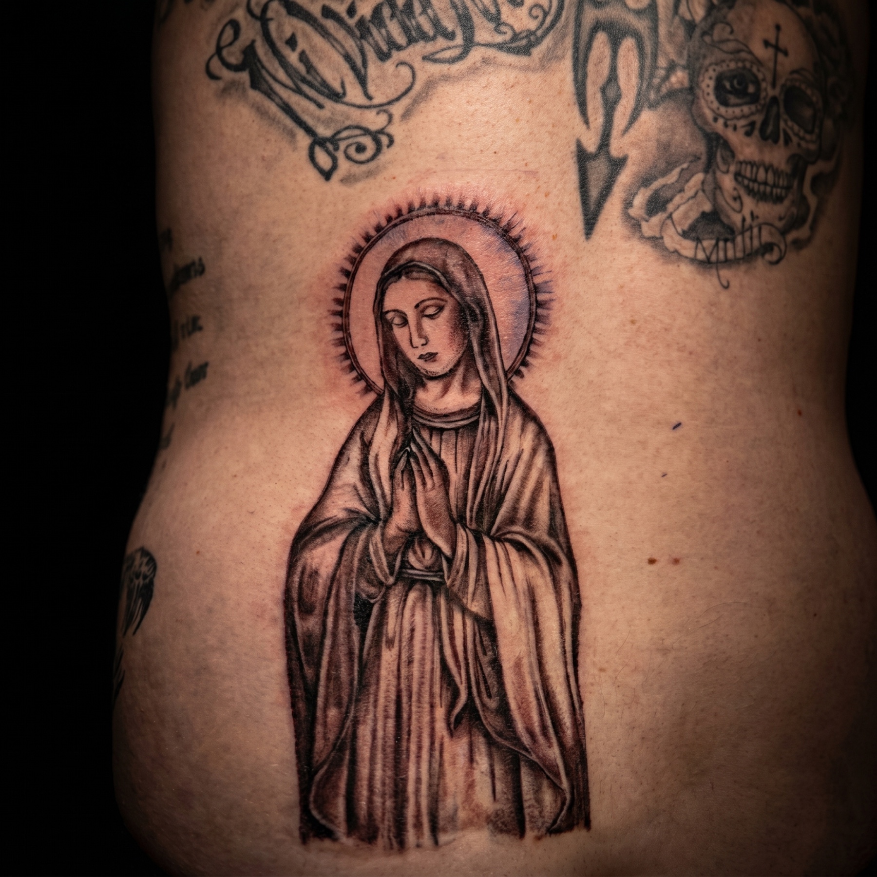Black and grey religious back piece of the Madonna with surrounding script