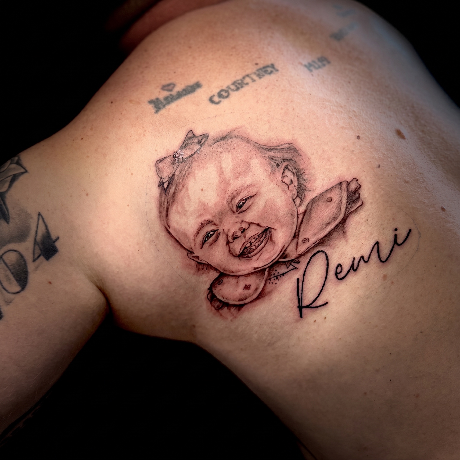 Black and grey memorial baby portrait with name in script on a shoulder